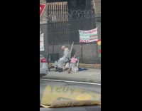 Man Wearing Stripes Sits on Sidewalk Next to Doll Baby in Pink 