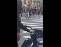 Shirtless man holding speaker waits to cross street 
