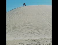 Guy rides yellow board down sand dune 