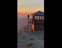 Man stands on the fire lookout railing at the mountains