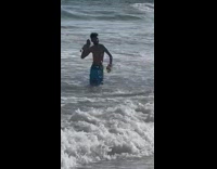 Guy standing in the water at the beach holding his timberland boots