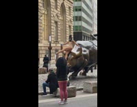 Woman sit bronze bull sculpture mask street.