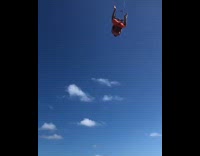 Collab risksIG - Guy orange shorts hangs upside down from handlebar on parachute at the beach