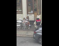 Two girls sit hold coffee outside shop