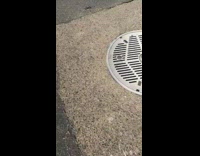 Small sinkhole ditch in the ground on pavement with orange cone inside