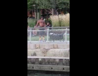 Shirtless man rides hoverboard backwards and pulls black wagon cart with speakers playing music in the park