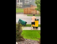 Guy collecting trash cans raining outside