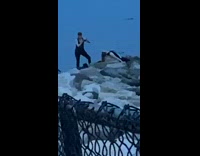 Girl leans against rocks by ocean water 