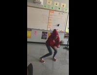 Girl in red high school hoodie and checkered Vans dances in front of a classroom