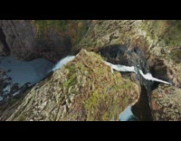 Drone flies straight down by waterfall cliff 
