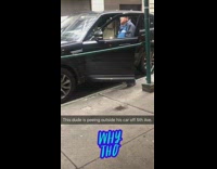 man pees outside his black car on sidewalk
