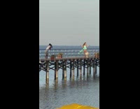 Woman in cyan dress models on the beach dock at sunset