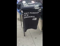 Lady sells explicit black shirts on sidewalk 