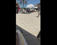 Blonde woman black bikini holds drink poolside