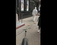 Person in white jumpsuit dragging prop hands on a chain on sidewalk