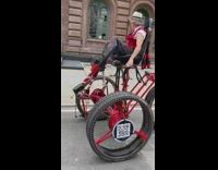 Old man on tall red tricycle inviting a woman on