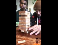 Guy successfully flicks bottom Jenga block off the table, jenga tower stands still, friends jaw drops