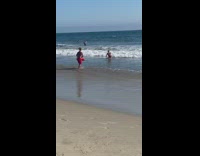 Shirtless guy red shorts runs towards ocean 