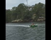 Guy rides green towable tube, turns and flies off tube and crashes into water