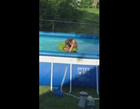 Person in green floatie in pool holding up dog pretending to paddle swim