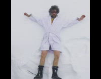 Guy in shower robe making snow angels in the snow outdoors 
