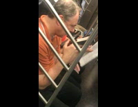 Man in orange shirt uses magnifying glass to read the newspaper