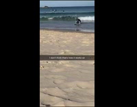 Collab Kook Of The Day - Black shirt guy stands on surfboard sand 