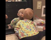 baby looking at itself in the mirror hits themselves on glass 