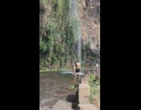 Woman in bikini raises hands in front of the waterfalls