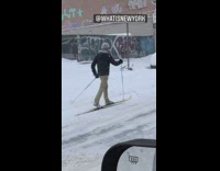 Guy in black jacket and tan pants cross country skiing on street
