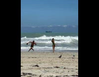 Woman in green bikini dances while man run around her at the beach