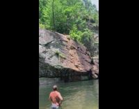 Guy dives backwards into water from cliff 