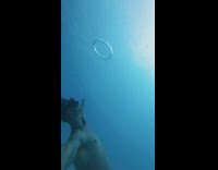 Guy takes snorkel off underwater blows air bubble ring 