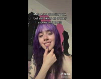 Girl pink shirt purple hair puts thumb on lip