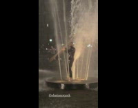 Guy wearing wetsuit stands in water fountain 