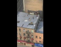 Two guys practice lassoing rooftop red awning 