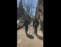 Two guys walking down sidewalk while operating remote control car