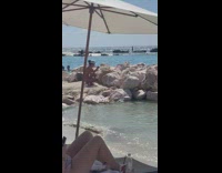 Woman pictures her drink on the beach rock