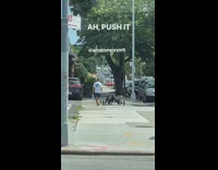 Guy in black rolls dumbbells on sidewalk with hands and feet 