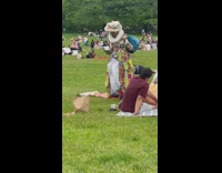 Person in Colorful Upcycled Dress Walks on Grass with Teacup 