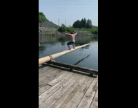 Guy runs off dock, jumps and balances on slippery pole then falls into water