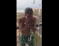 Shirtless guy on hotel balcony in turquoise shorts smashing beer on forehead and spraying glass door