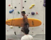 Shirtless surfer with board comes out from rock climbing wall 
