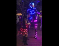 Man and woman dressed in rainbow neon lights costume and stilts pose next to pedestrian