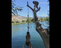 Girl on top of tree branch jumps on top of other girl swinging into water