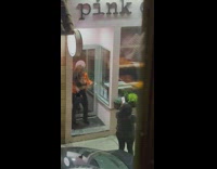 Woman in orange jacket and bra underneath poses in front of a store