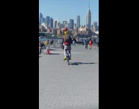Guy drives bicycle while ball balance on his head at the park 