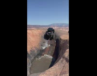 Black ATV climbs up side of rock and out of water