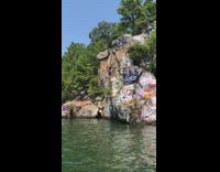 Guy backflips off cliff with graffiti and belly flops into water