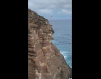 Guy in pink swimming trunks jumps off very tall cliff and dives into the ocean